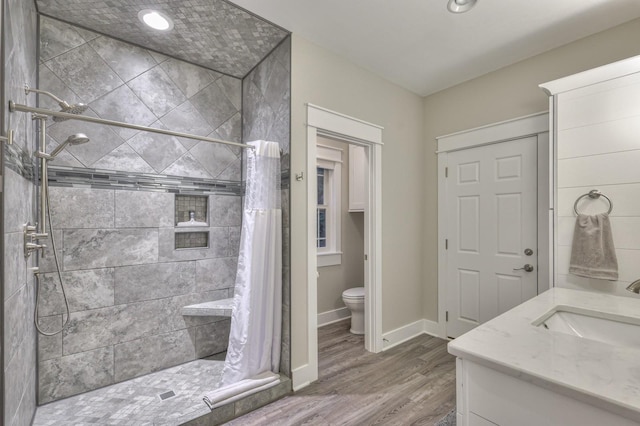 bathroom featuring toilet, a stall shower, vanity, wood finished floors, and baseboards