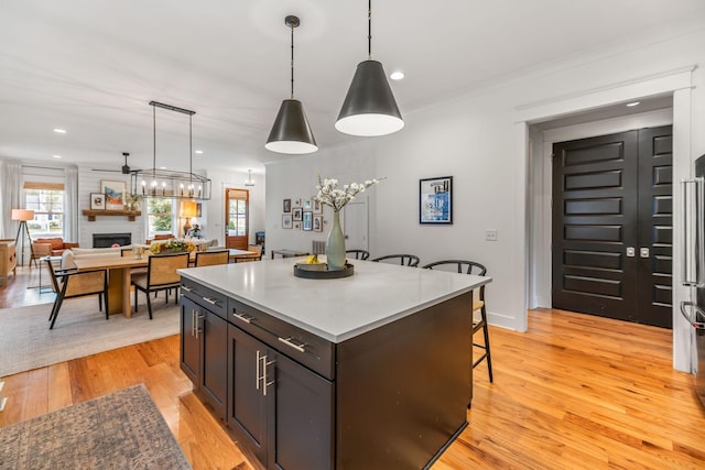 kitchen featuring a large fireplace, a kitchen island, open floor plan, hanging light fixtures, and light wood finished floors