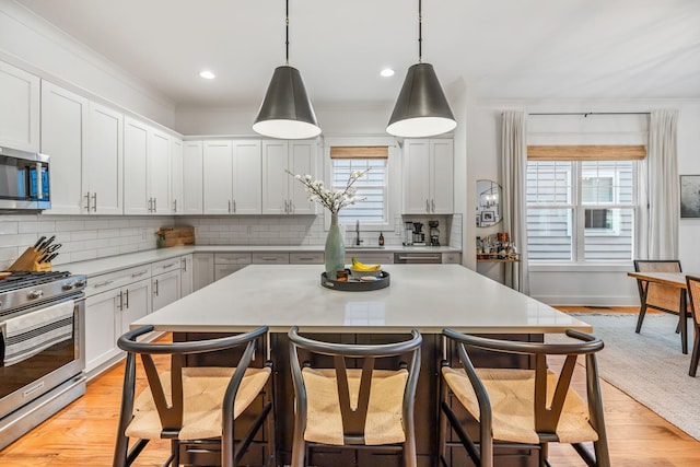 kitchen featuring light countertops, appliances with stainless steel finishes, hanging light fixtures, and white cabinets