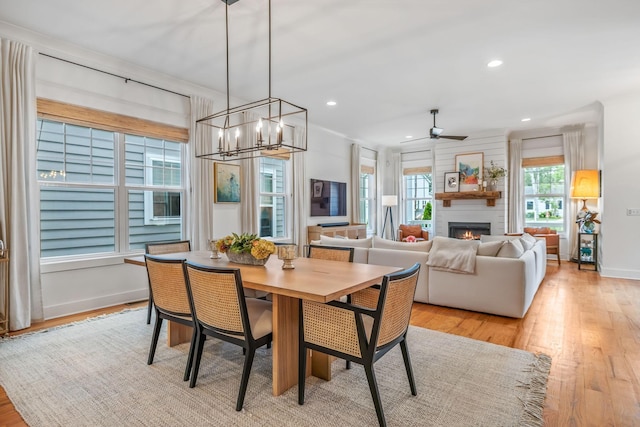 dining room featuring a warm lit fireplace, ceiling fan with notable chandelier, light wood-style flooring, and recessed lighting