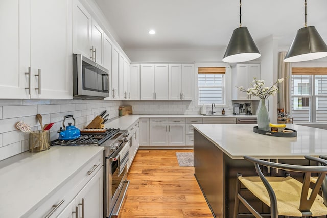 kitchen featuring stainless steel appliances, white cabinetry, light countertops, light wood finished floors, and decorative light fixtures