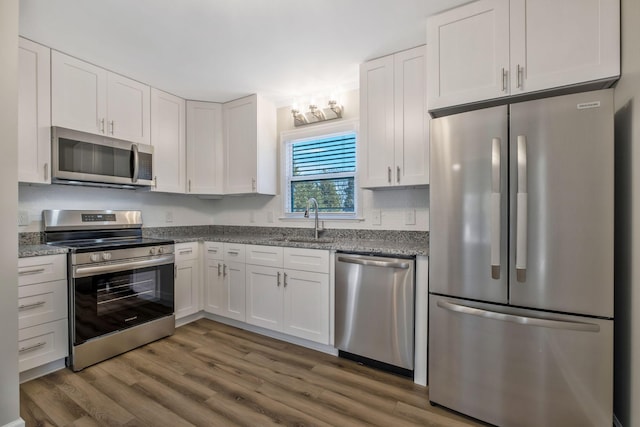 kitchen with dark wood-style floors, white cabinetry, stainless steel appliances, and light stone counters