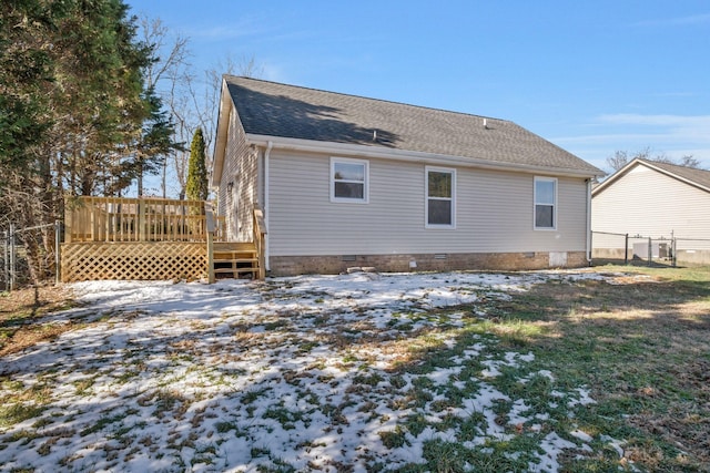 snow covered house with a deck, roof with shingles, crawl space, and fence