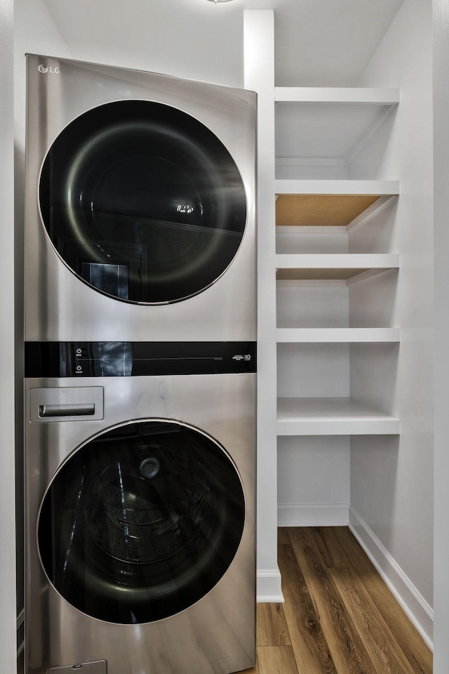 laundry room with stacked washer and dryer, wood finished floors, laundry area, and baseboards