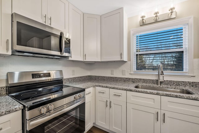 kitchen featuring stainless steel appliances, white cabinets, a sink, and light stone countertops