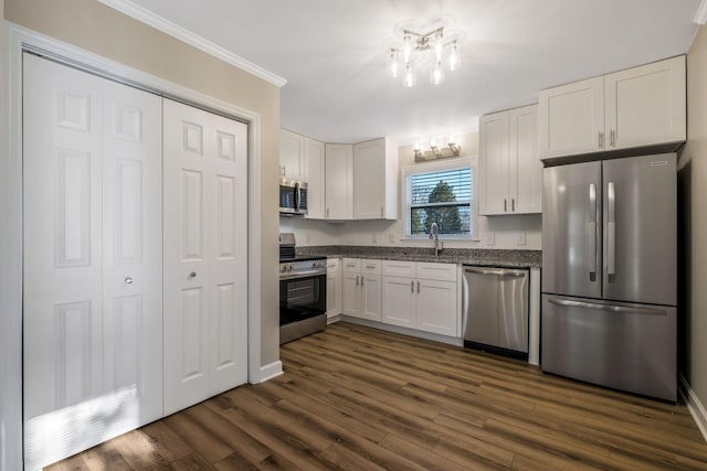 kitchen featuring dark wood-style flooring, crown molding, appliances with stainless steel finishes, white cabinets, and a chandelier