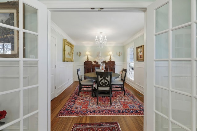 dining room with a wainscoted wall, crown molding, a decorative wall, an inviting chandelier, and wood finished floors