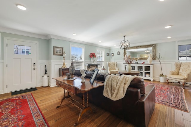 living area with wainscoting, wood finished floors, crown molding, a fireplace, and recessed lighting