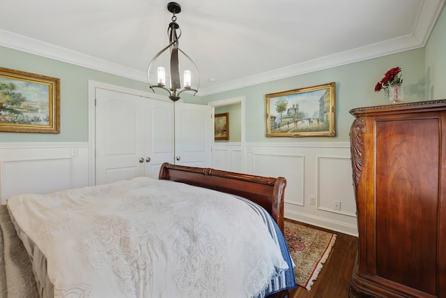 bedroom featuring dark wood-style flooring, a wainscoted wall, crown molding, a notable chandelier, and a decorative wall