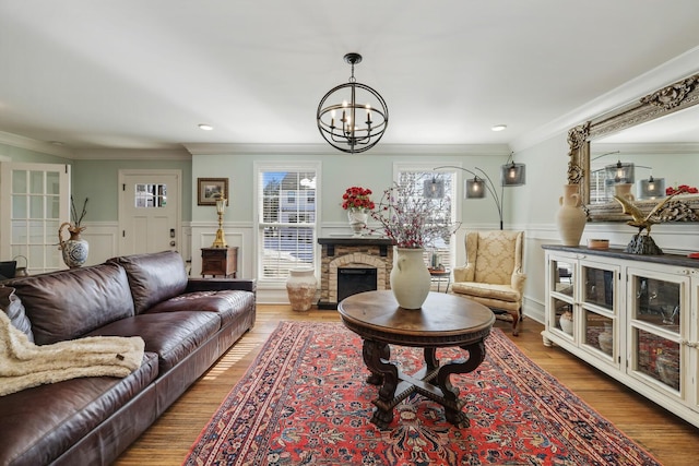 living room featuring wainscoting, ornamental molding, wood finished floors, a fireplace, and a notable chandelier