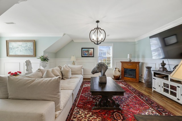 living area with a wainscoted wall, crown molding, visible vents, a glass covered fireplace, and wood finished floors