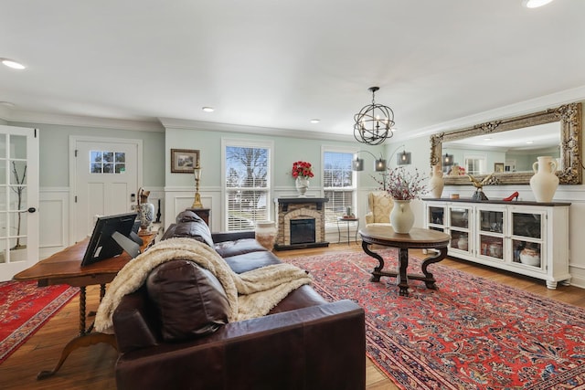 living area featuring a stone fireplace, a decorative wall, a wainscoted wall, wood finished floors, and ornamental molding