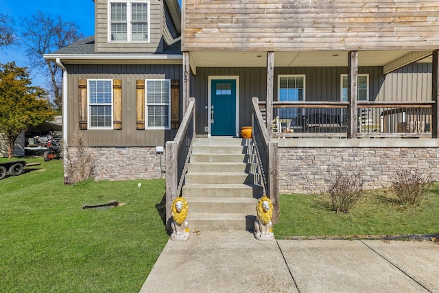 entrance to property featuring board and batten siding, covered porch, roof with shingles, and a lawn