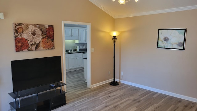 interior space featuring light wood finished floors, ornamental molding, vaulted ceiling, and baseboards