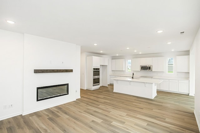 kitchen with white cabinets, a kitchen island with sink, stainless steel appliances, light countertops, and a sink