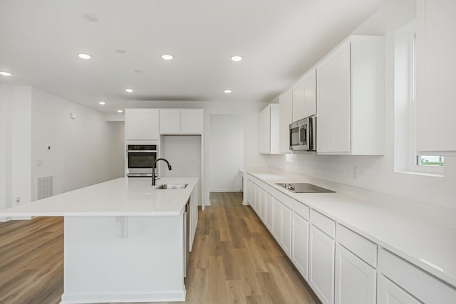 kitchen with light countertops, appliances with stainless steel finishes, a kitchen island with sink, and white cabinets