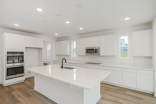 kitchen with a center island with sink, stainless steel appliances, a sink, and light countertops