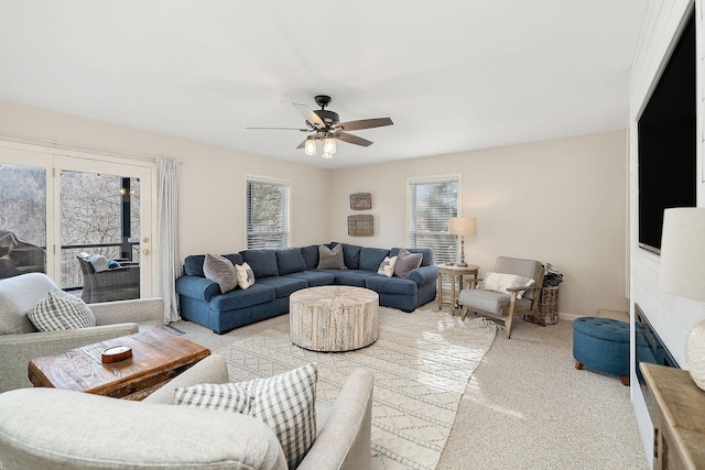 living room with light carpet, baseboards, a ceiling fan, and a glass covered fireplace