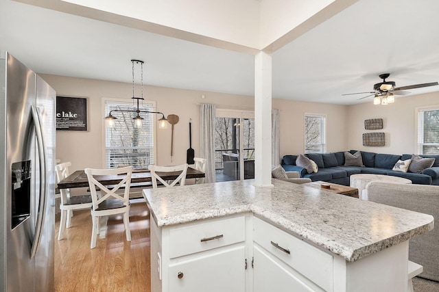 kitchen with white cabinets, stainless steel fridge with ice dispenser, open floor plan, decorative light fixtures, and light wood-type flooring