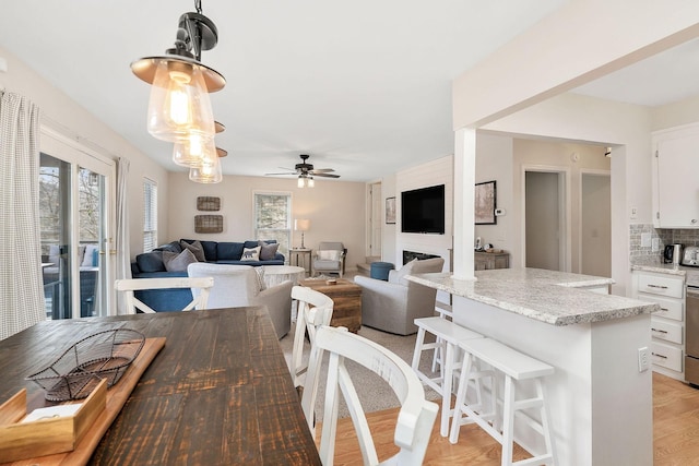 dining area featuring light wood-style flooring, a fireplace, and a ceiling fan