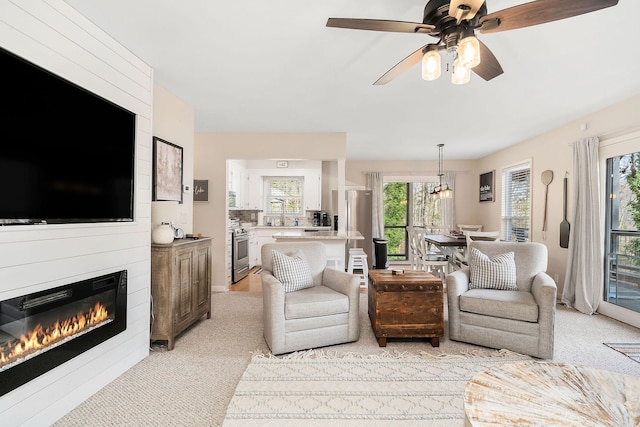 living area featuring a glass covered fireplace, light colored carpet, and ceiling fan