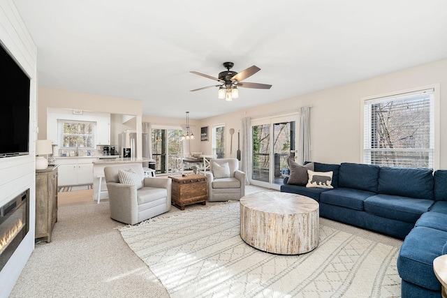 living area with a ceiling fan and a glass covered fireplace