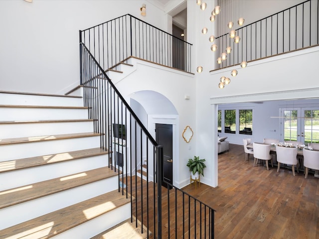 staircase with french doors, a towering ceiling, baseboards, and wood finished floors