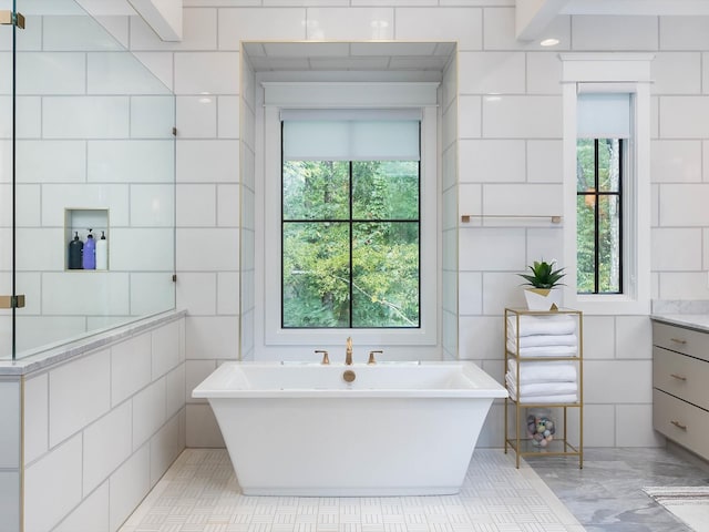 full bathroom with vanity, a freestanding tub, and tile walls