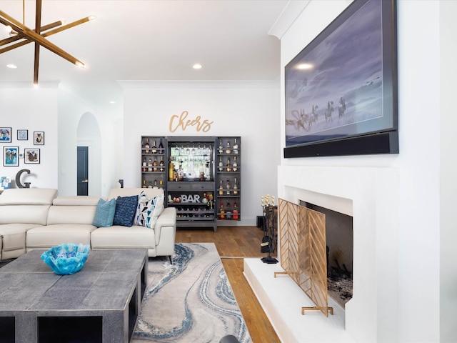 living area featuring arched walkways, recessed lighting, a fireplace with raised hearth, ornamental molding, and wood finished floors