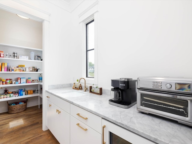 kitchen with a toaster, dark wood finished floors, light stone counters, white cabinetry, and a sink