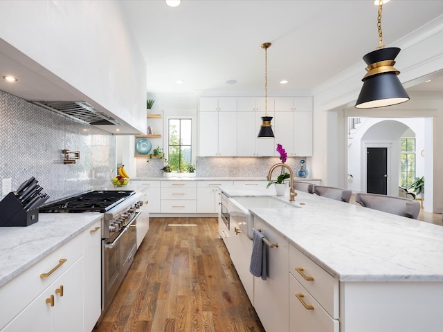 kitchen featuring a sink, white cabinets, double oven range, an island with sink, and island exhaust hood