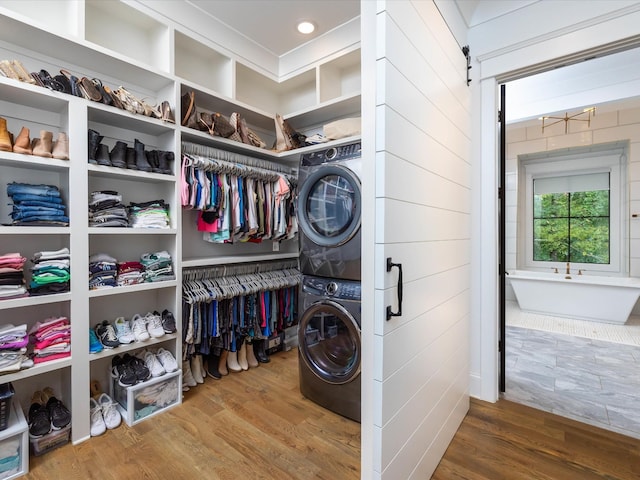 clothes washing area featuring laundry area, a barn door, stacked washer and dryer, and wood finished floors