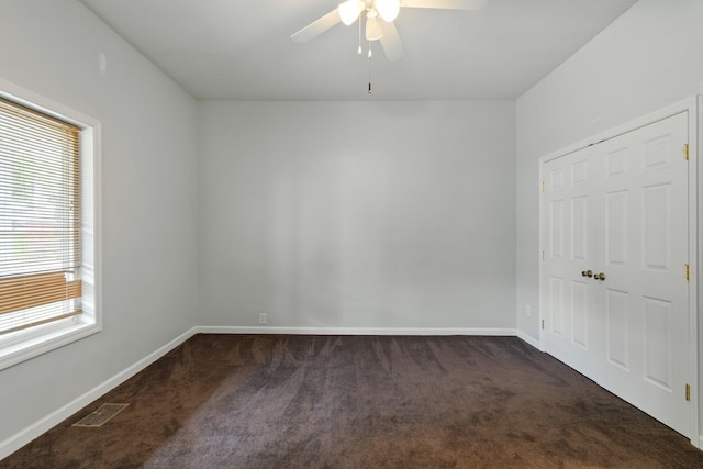 empty room with dark carpet, visible vents, and baseboards