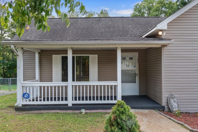 doorway to property featuring covered porch and roof with shingles