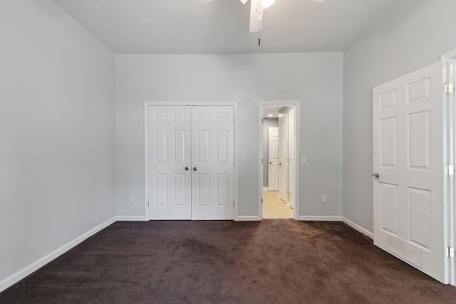 unfurnished bedroom with baseboards, visible vents, dark carpet, and a closet