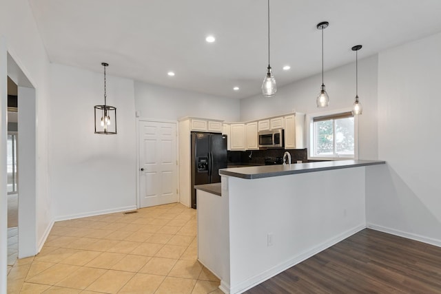 kitchen with a peninsula, white cabinetry, hanging light fixtures, stainless steel microwave, and dark countertops