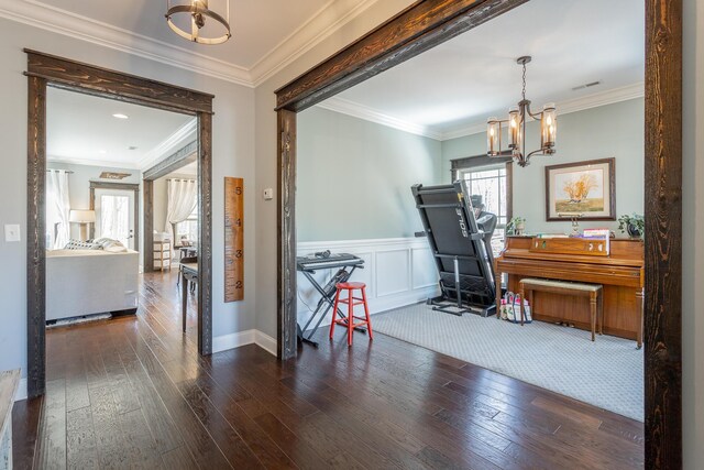 interior space featuring dark wood-style floors, ornamental molding, a notable chandelier, and wainscoting