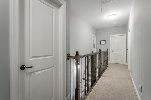 hall with light carpet, attic access, baseboards, and an upstairs landing