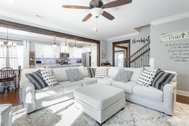 living room with ornamental molding, light wood-style flooring, baseboards, and ceiling fan with notable chandelier