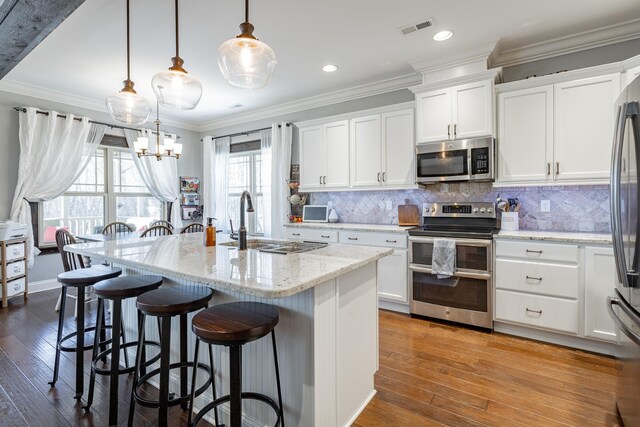 kitchen featuring decorative light fixtures, visible vents, white cabinetry, appliances with stainless steel finishes, and a center island with sink