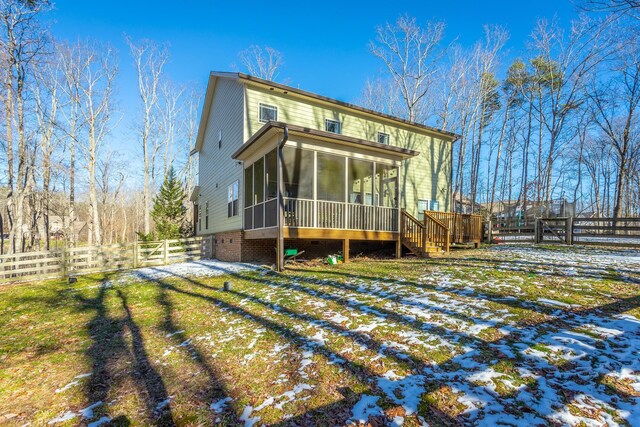 snow covered rear of property with a garage, a sunroom, a fenced backyard, and a yard