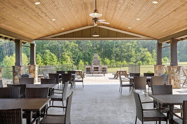 view of patio / terrace featuring a ceiling fan, outdoor dining space, an outdoor stone fireplace, and fence