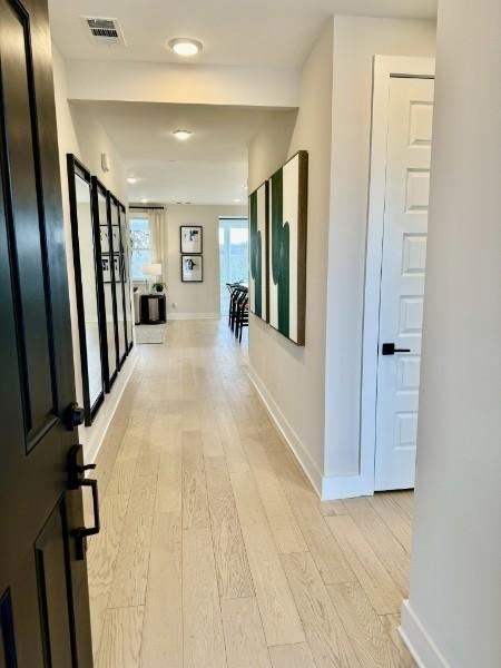 hall featuring visible vents, light wood-style flooring, and baseboards