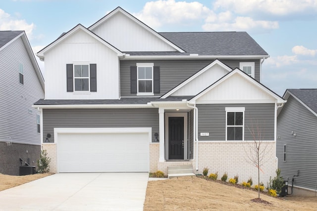 view of front facade with driveway, a shingled roof, a garage, brick siding, and central AC unit