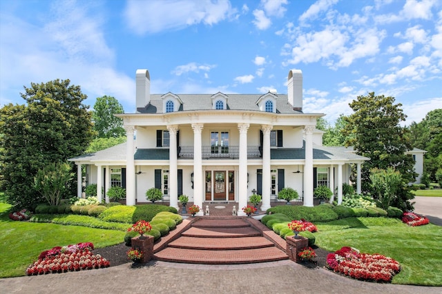 view of front facade with a chimney, a balcony, and a front lawn