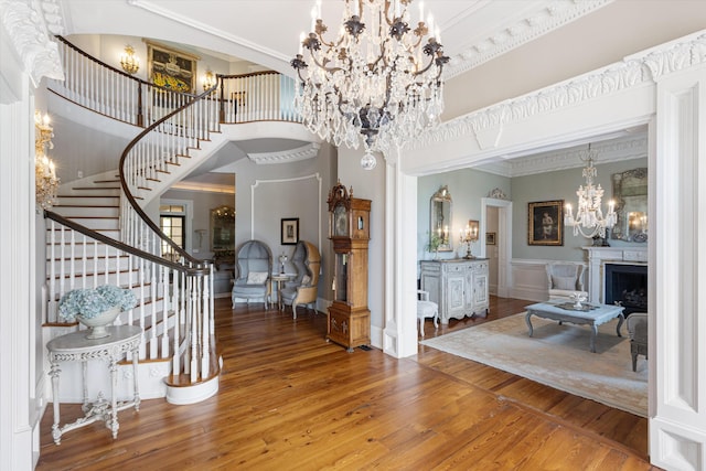 foyer featuring crown molding, a fireplace, a notable chandelier, stairway, and wood finished floors