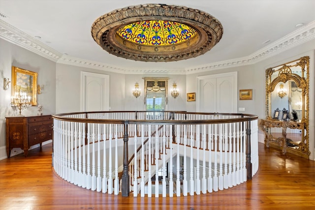 corridor featuring crown molding, a raised ceiling, wood finished floors, and an upstairs landing