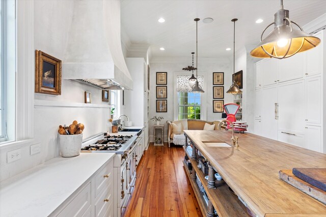 kitchen featuring stainless steel stove, a sink, white cabinetry, custom exhaust hood, and decorative light fixtures