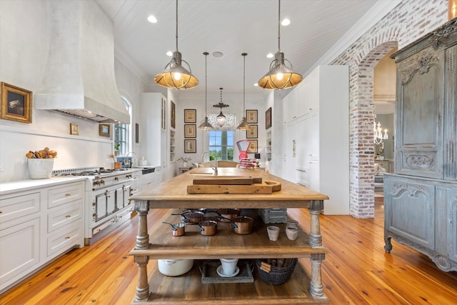 kitchen with pendant lighting, stainless steel gas cooktop, light countertops, ornamental molding, and white cabinets