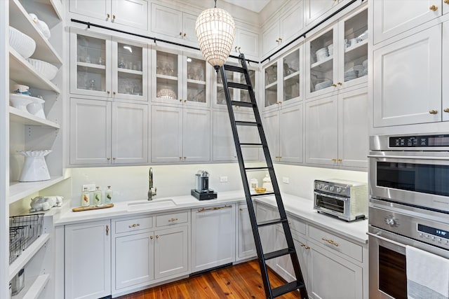 kitchen with light countertops, hanging light fixtures, double oven, glass insert cabinets, and a sink